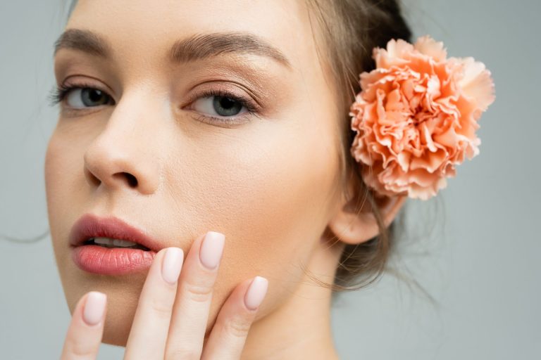 close up portrait of sensual woman with natural makeup and peach carnation behind ear touching face
